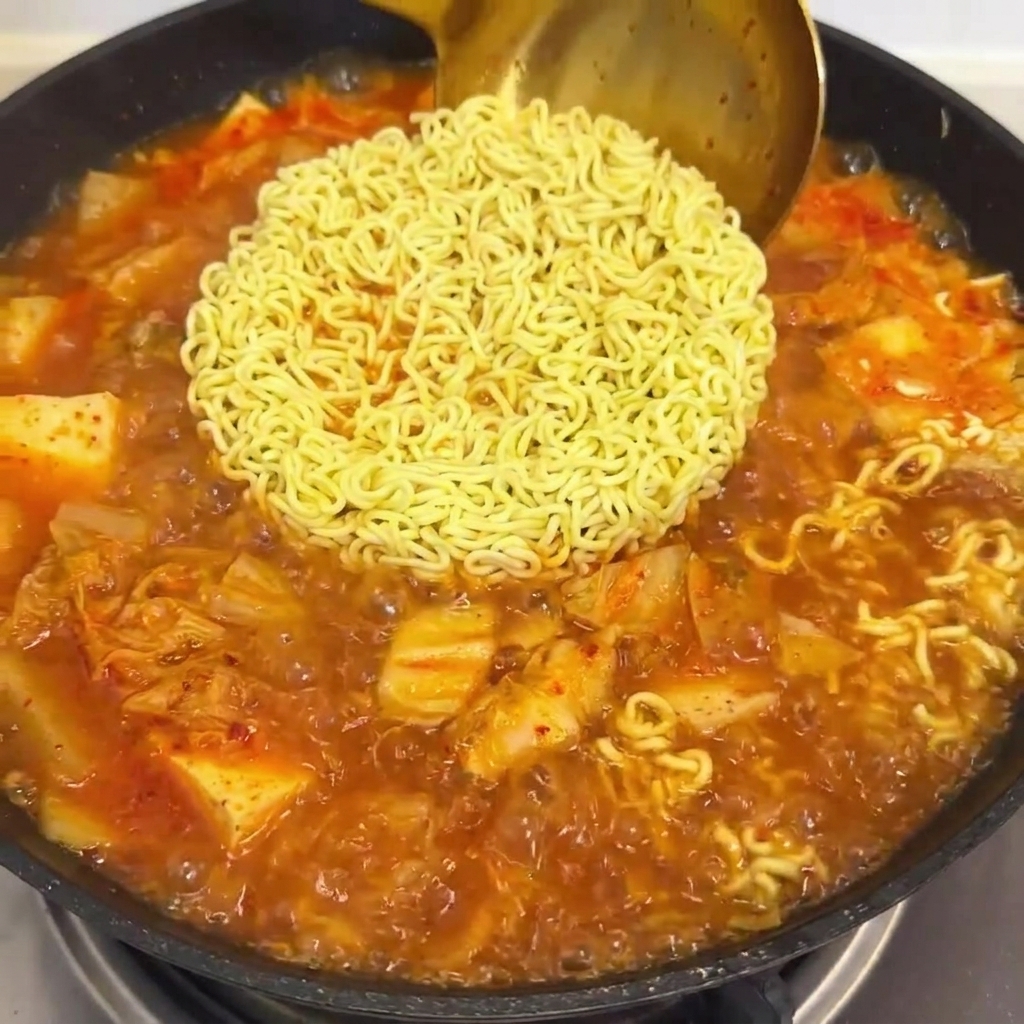 沸騰したラーメンとキムチスープの入った鍋に、赤いソースを注いでいる様子。