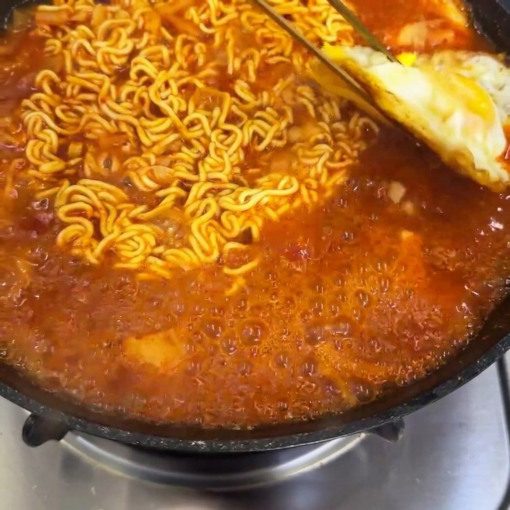 ぐつぐつ煮えるスパイシーなラーメンの上に、目玉焼きをのせている様子。