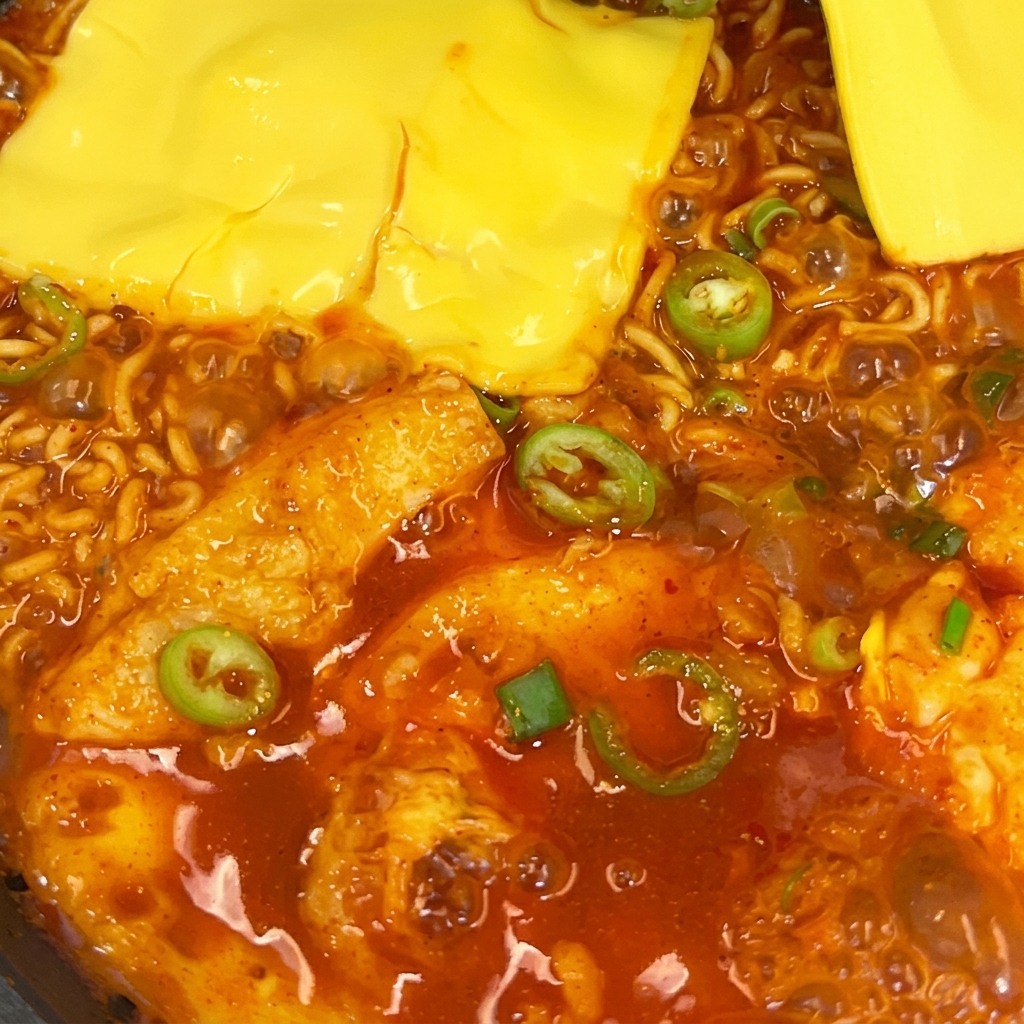 フライパンの中のスパイシーなラーメンの上で、2枚の黄色いスライスチーズが溶けている様子。