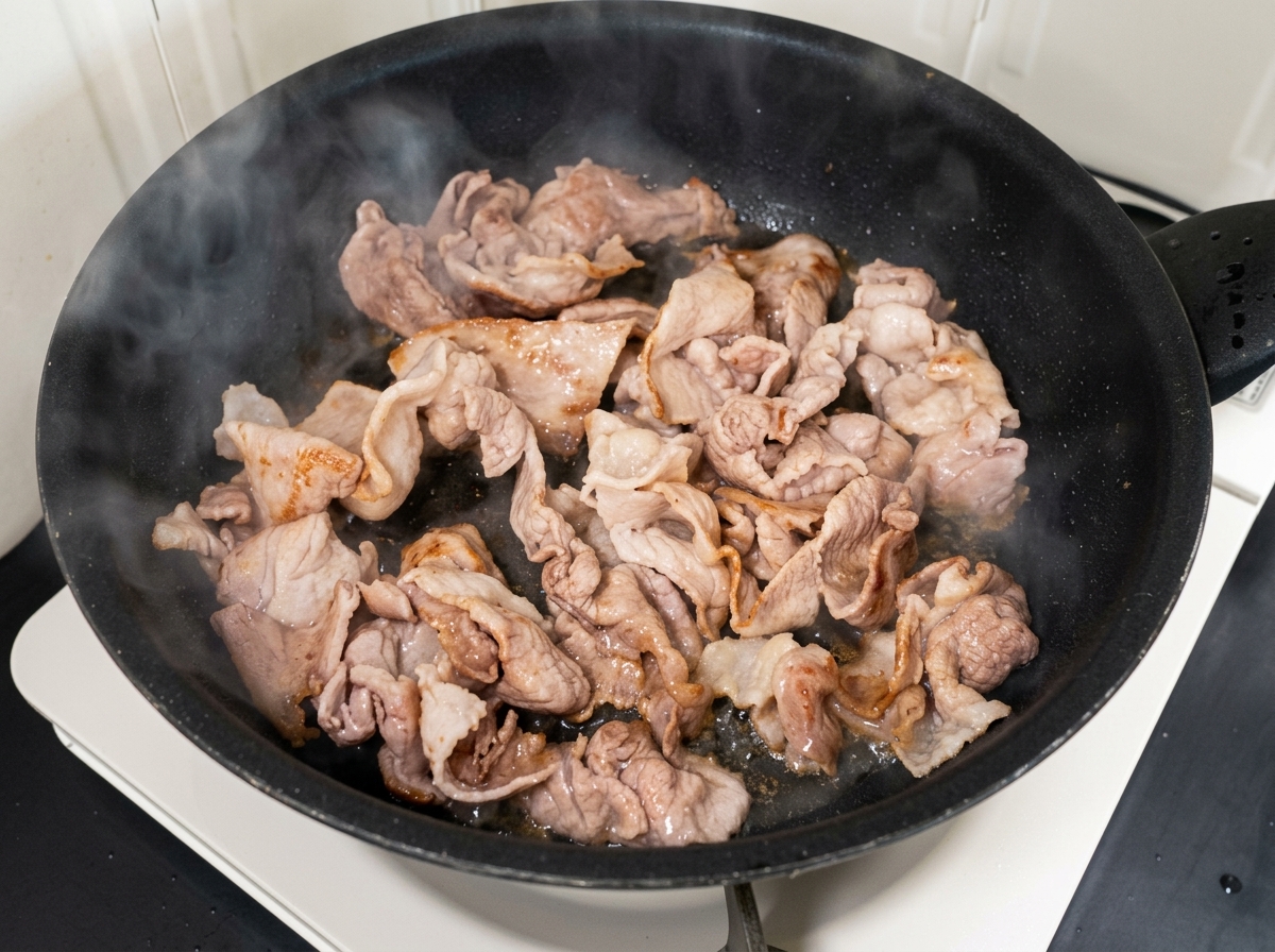 炒めた豚肉にキムチと砂糖を加えて混ぜ合わせている様子。
