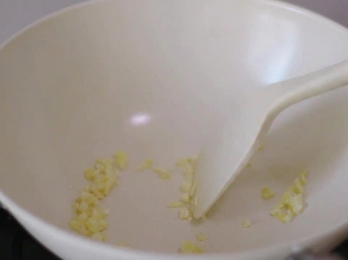 白いフライパンで刻んだ椎茸とにんにくをヘラで炒めている様子。