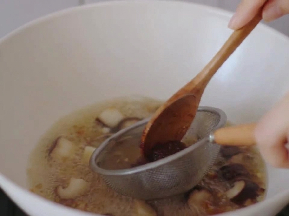 小さなザルと木べらを使って、沸騰したスープに味噌を溶かしている様子。