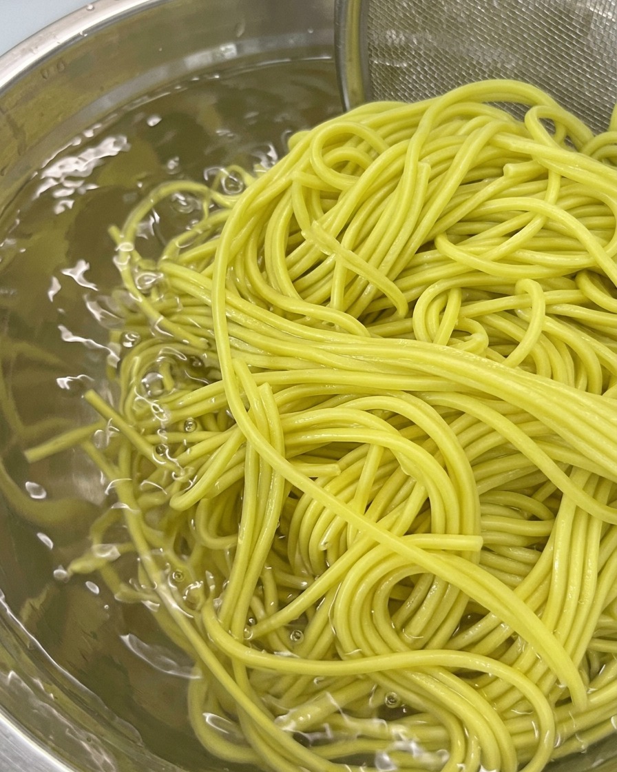 ザルに入れた麺をボウルに入った冷水で洗っている様子。