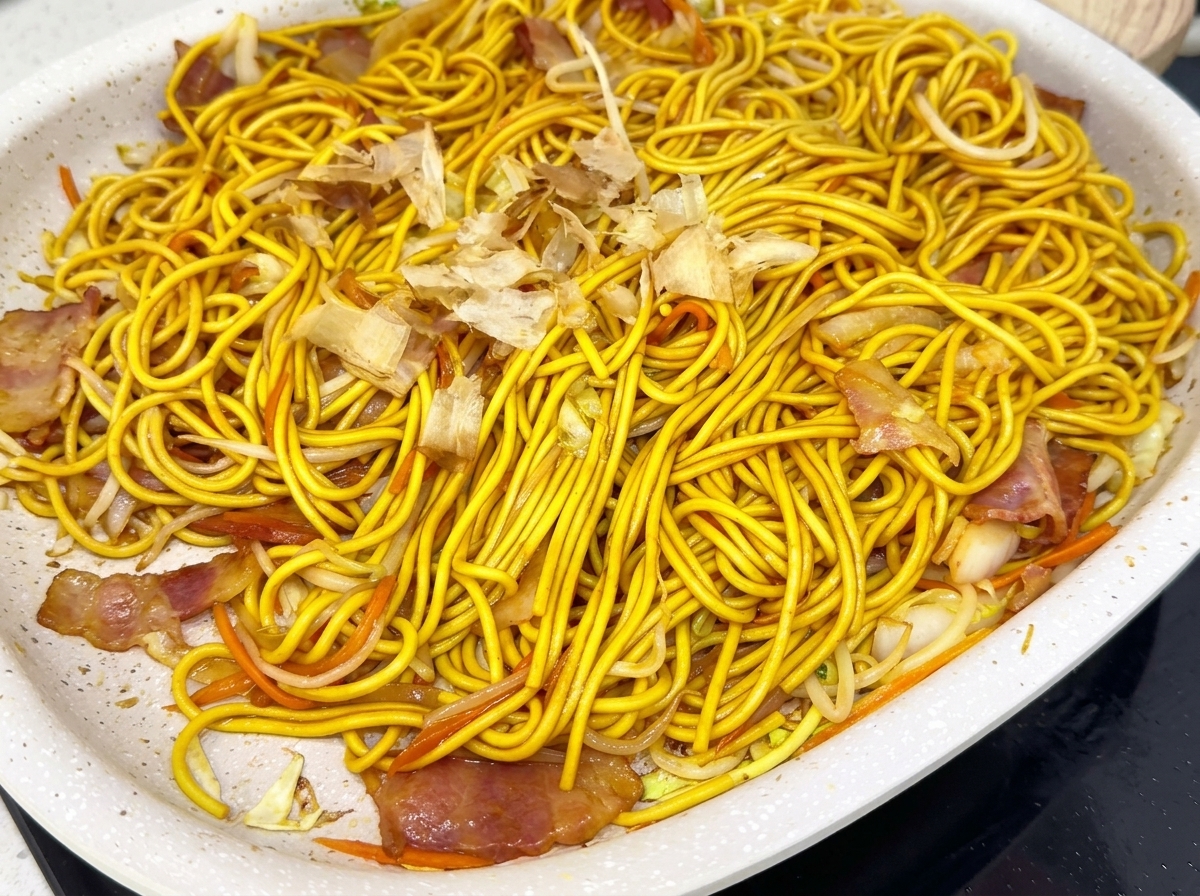 器に盛り付けた焼きそばにかつお節を振りかけている様子。