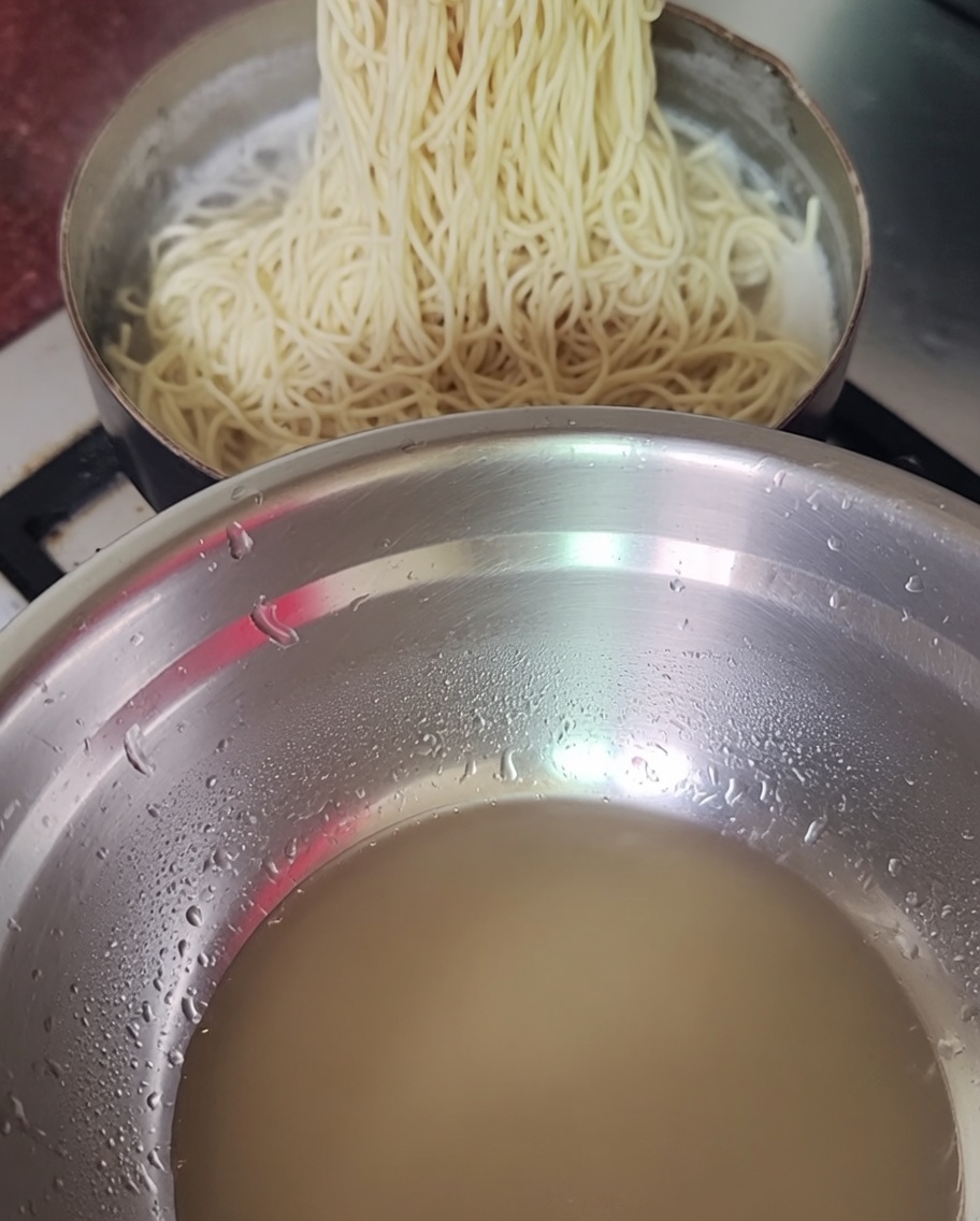 茹で上がった麺をお湯から箸で引き上げている様子