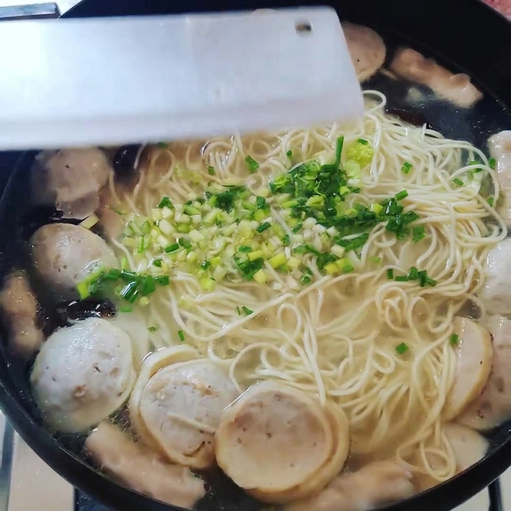 麺や具材が入った鍋に刻んだ青ねぎを散らしている様子を上から見た図