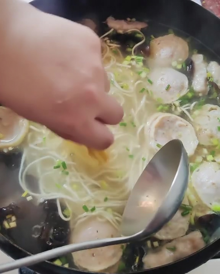 調理済みの麺とスープが入った鍋に薄切りのレモンを手で並べている様子
