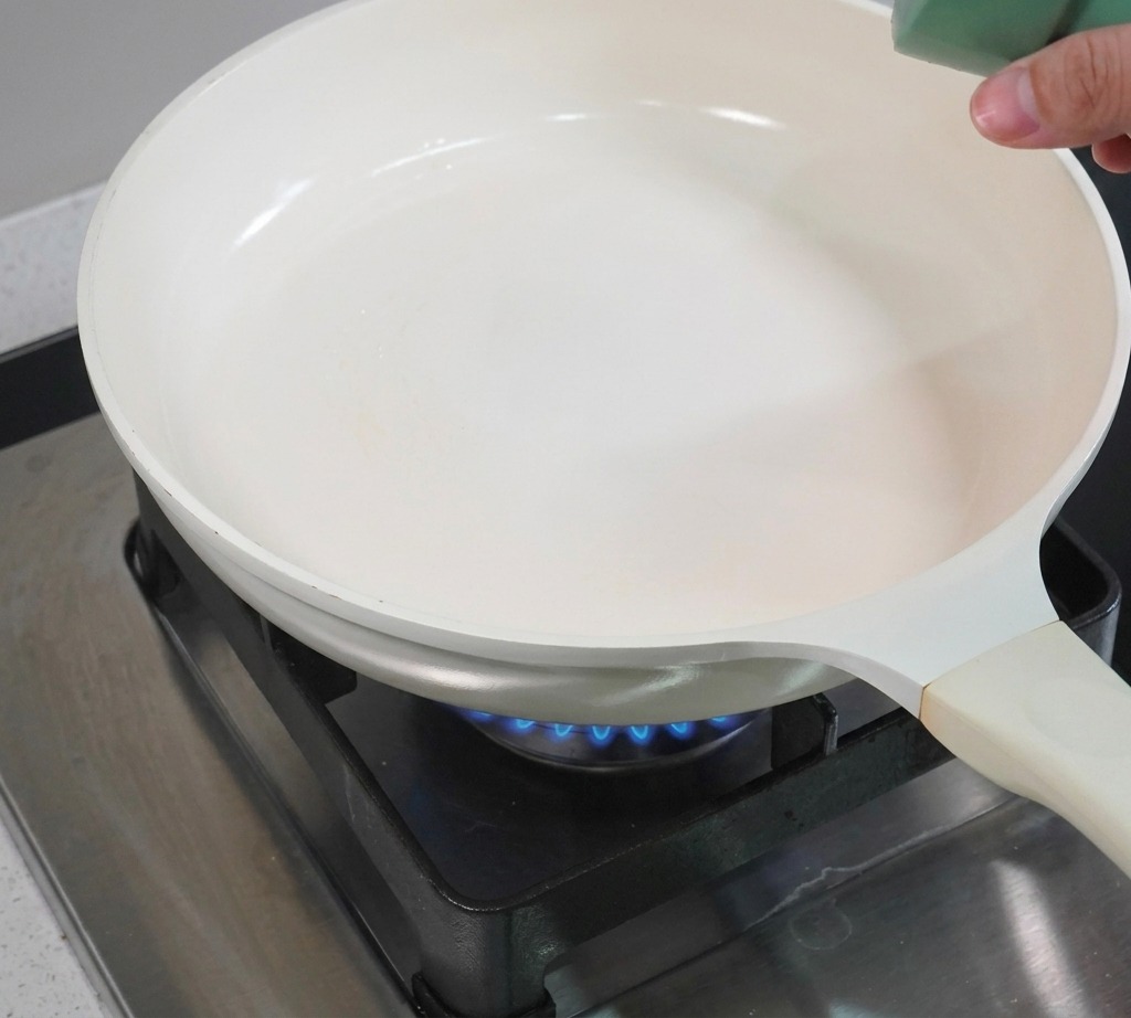 白いノンスティック加工のフライパンでスパムのスライスを焼き、表面に美味しそうな焼き色がついている様子。