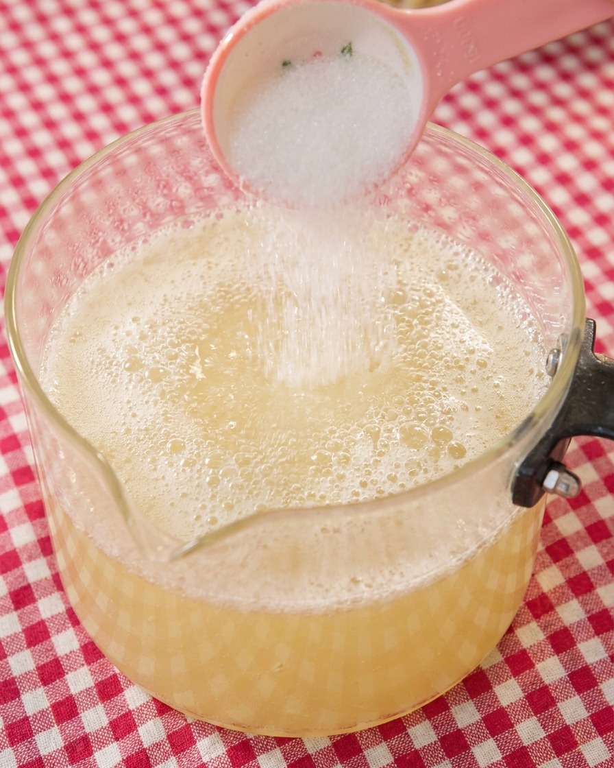 煮立っているラーメンスープに、スプーンで砂糖を少量加える様子。