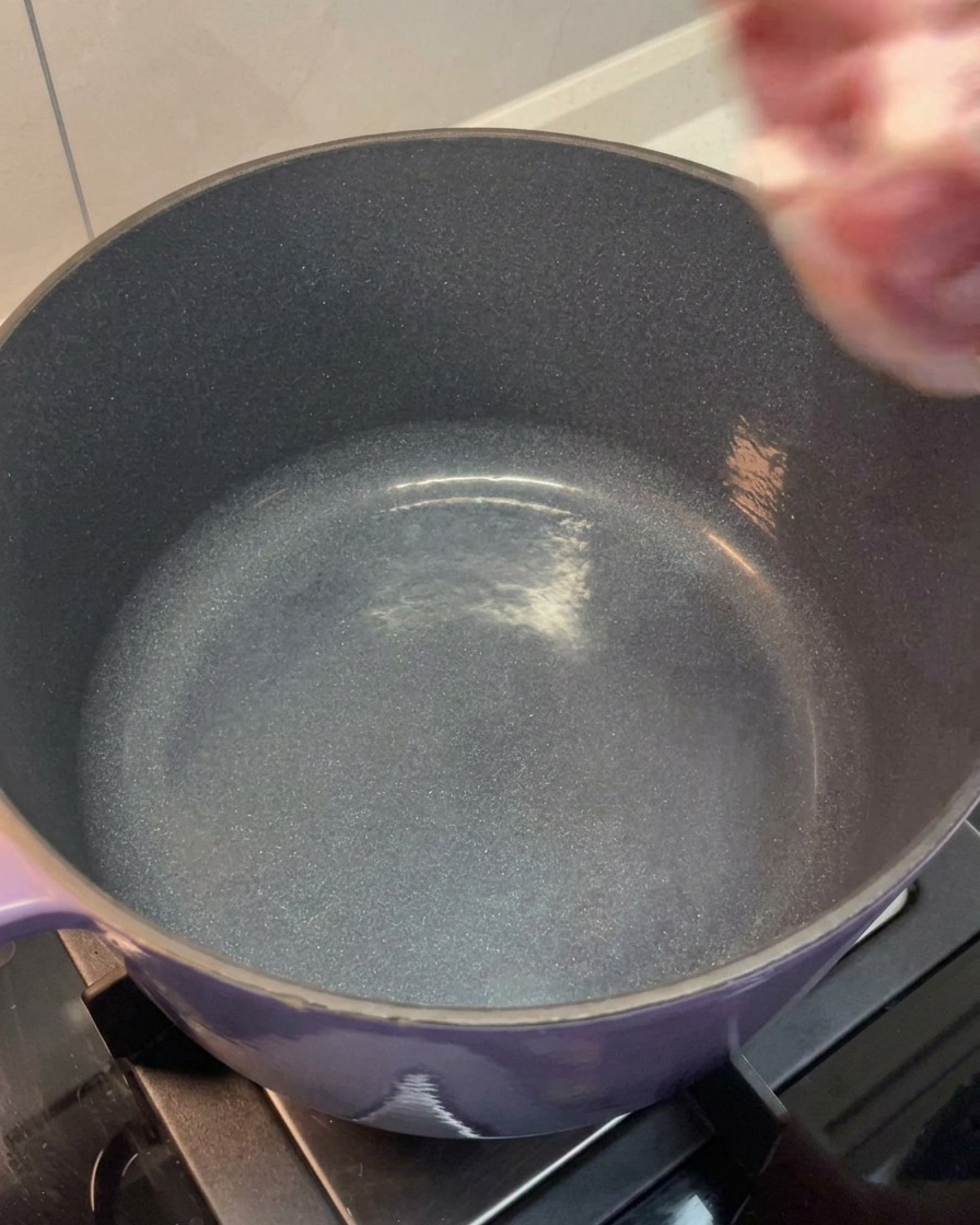大きな鍋に洗った豚肉と骨を入れる様子