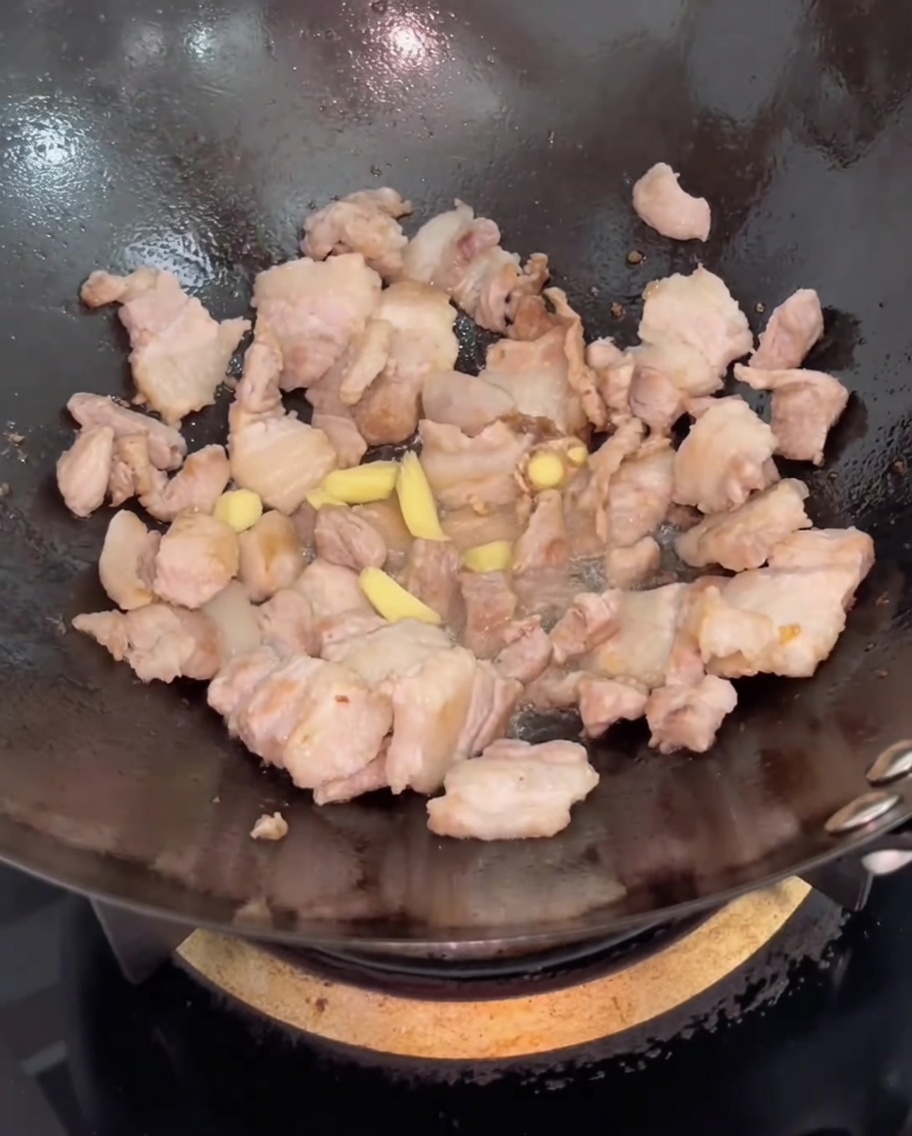 豚バラ肉に生姜のスライスを加えて炒める様子。