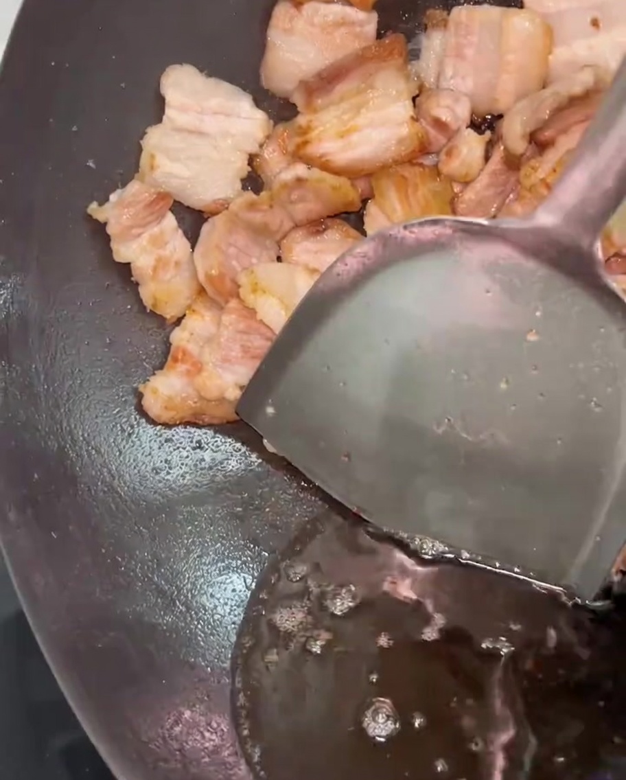ヘラで肉を寄せ、鍋から余分な脂を流し出している様子。