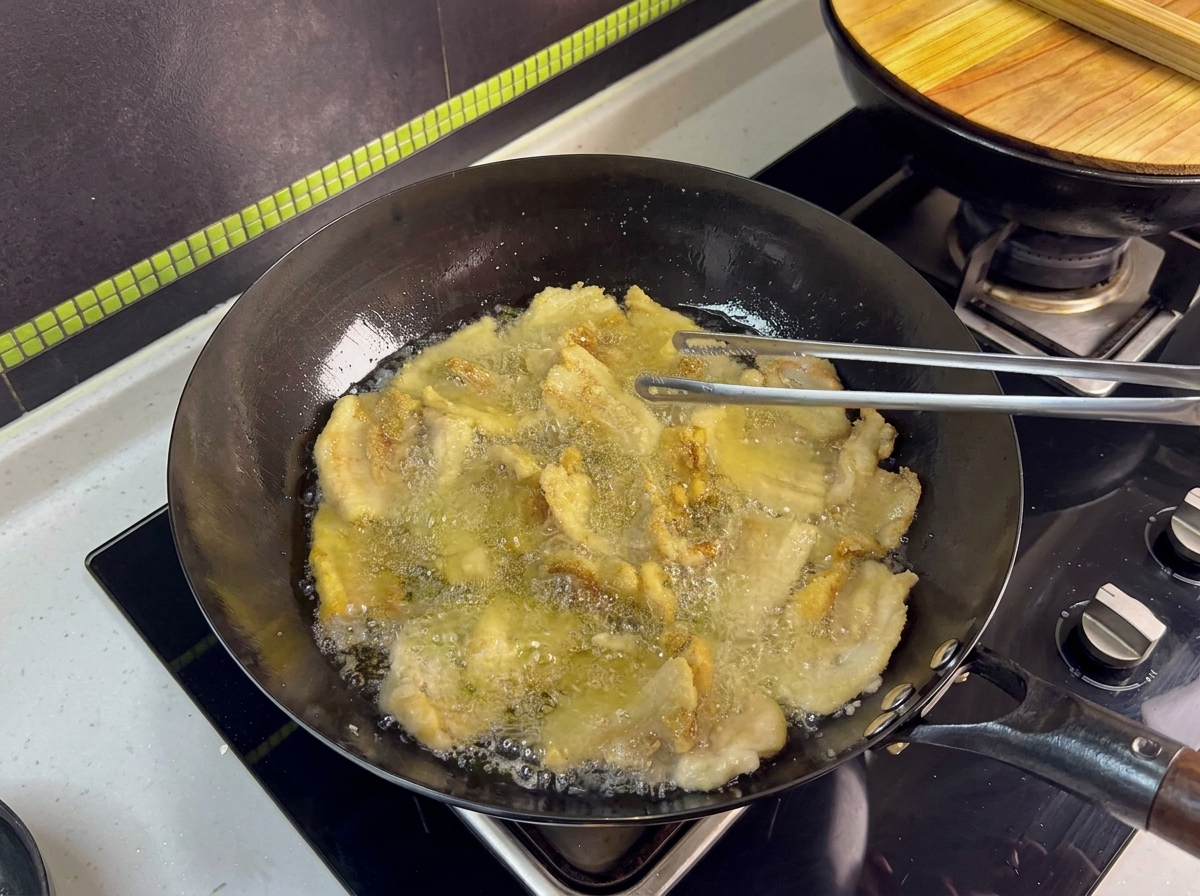 中華鍋で豚バラ肉をトングで返しながら揚げている様子