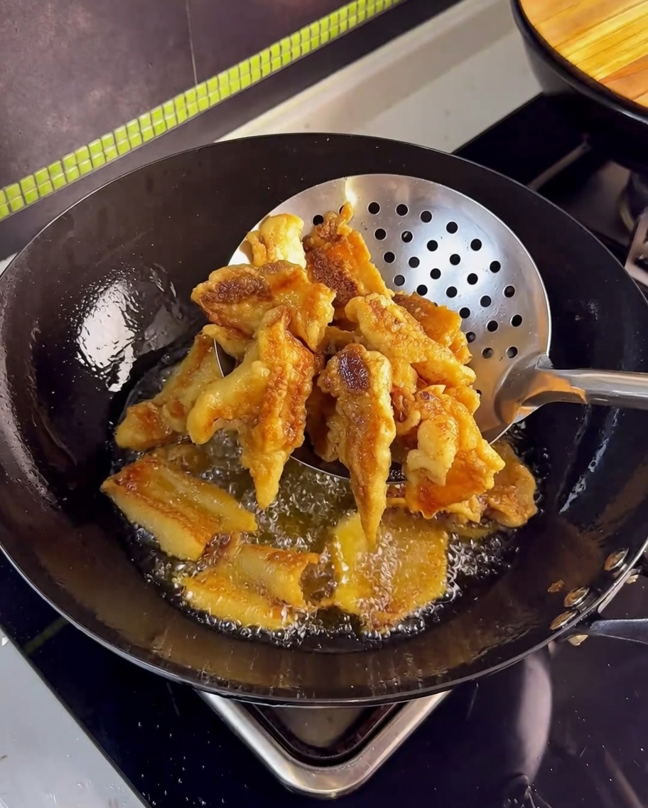 揚げ上がったカリカリの豚バラ肉を網じゃくしですくい上げている様子