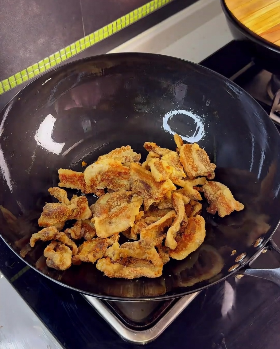 中華鍋で揚げた豚肉とニンニクをたれと絡めている様子