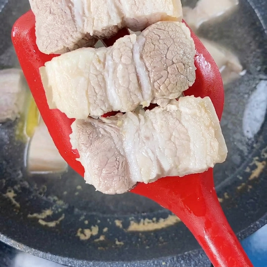 赤いスパチュラで茹で上がった豚肉をすくい上げている様子。