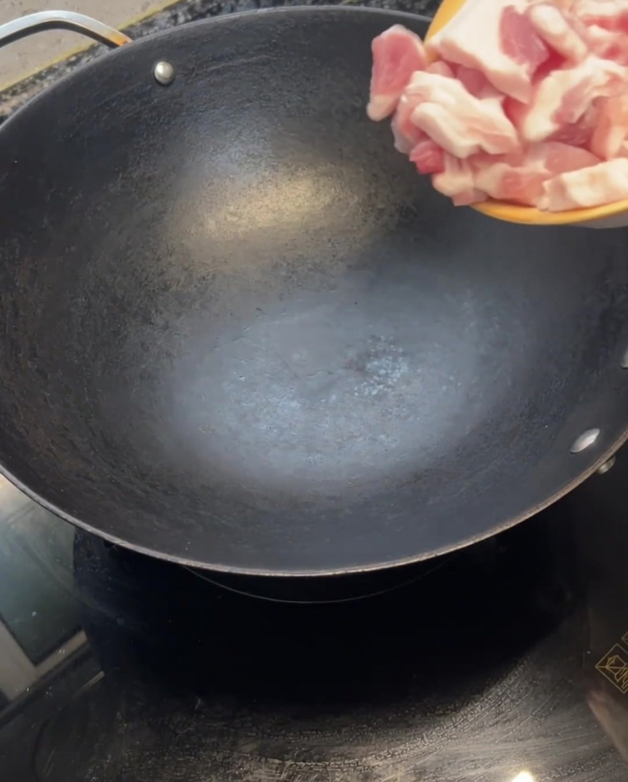 熱したフライパンにスライスした生の豚バラ肉を入れている様子。