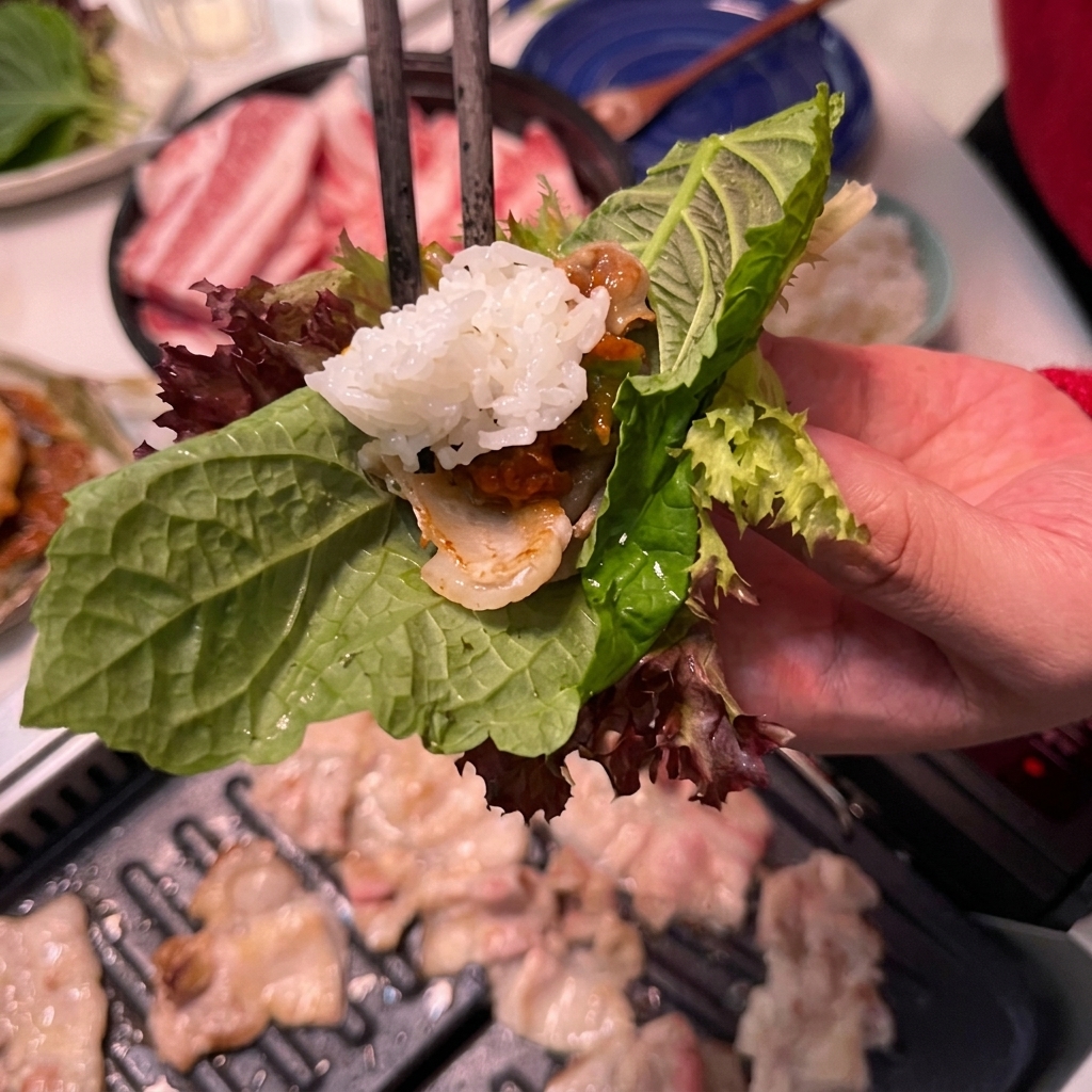 サンチュの上の肉にスプーンでご飯をのせている様子。