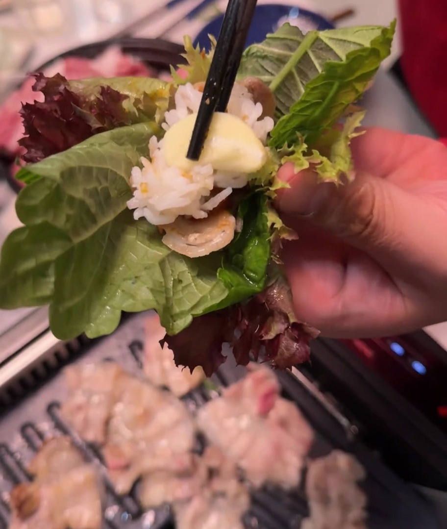 豚肉、ご飯、サムジャン、ニンニクがのった葉を包んでいる手元。