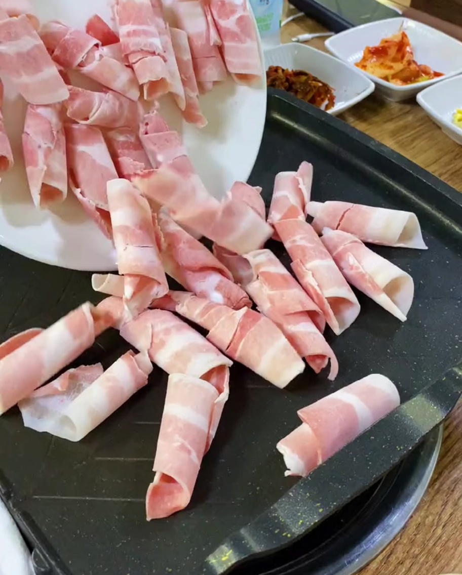 熱い鉄板に並べられた生の豚バラ薄切り肉。