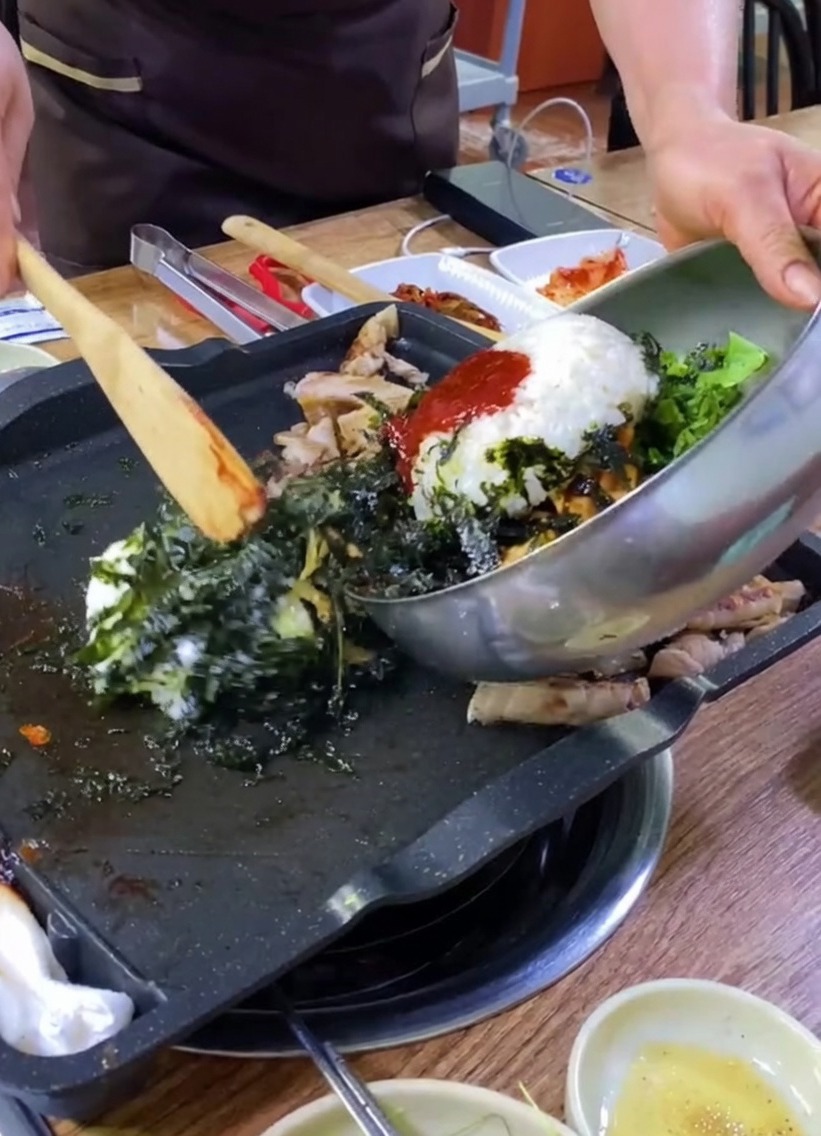 金属製のボウルから鉄板へ、ご飯、野菜、海苔が移される様子。