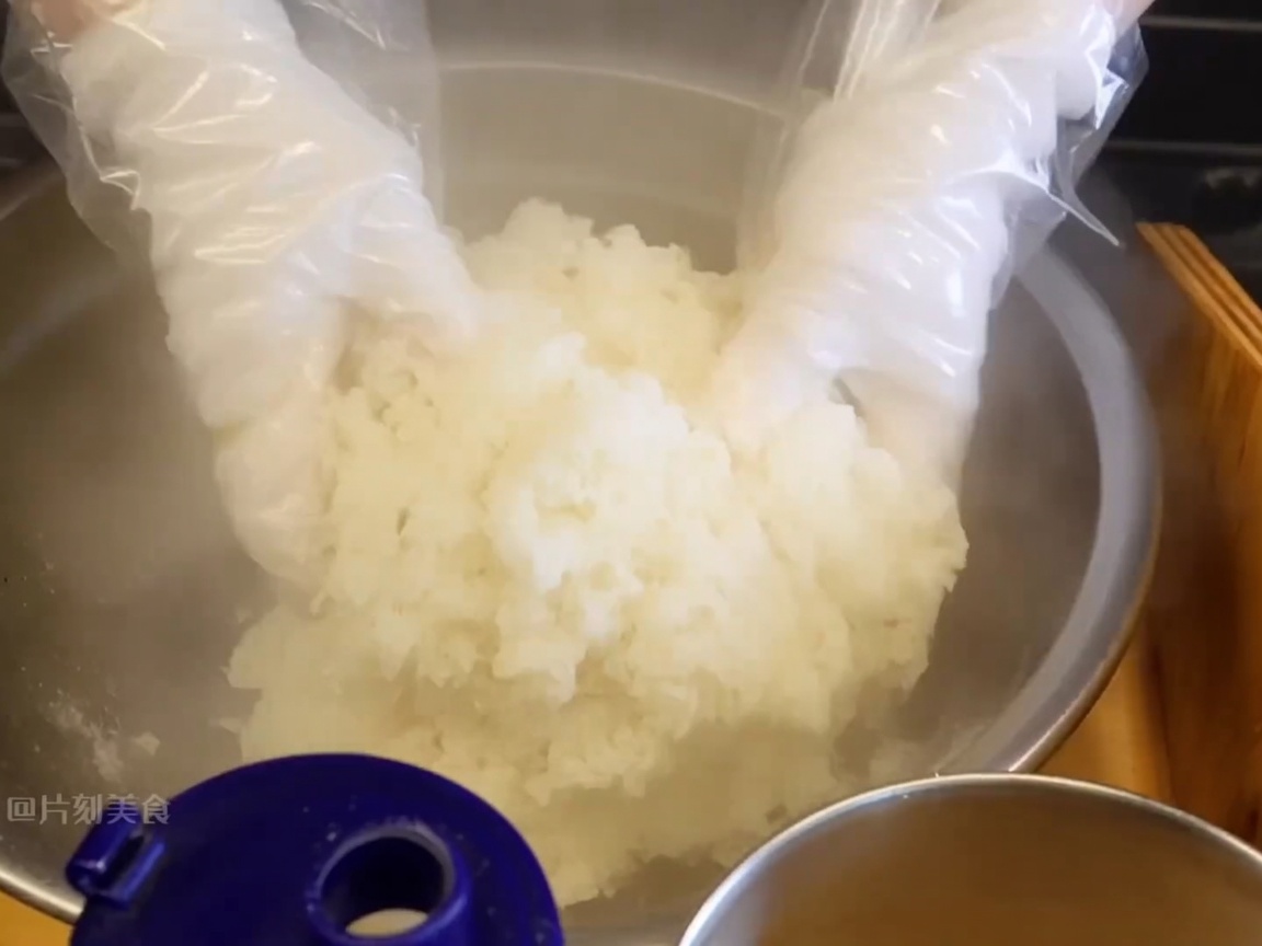 手袋をはめた手で、温かいご飯と調味料を素早く混ぜ合わせている様子。