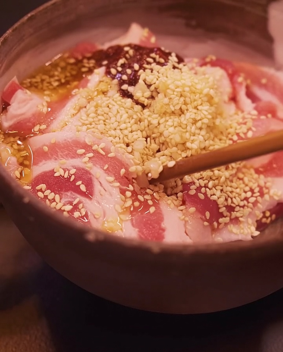 箸を使ってボウルの中の豚バラ肉と調味料を混ぜ合わせている様子。