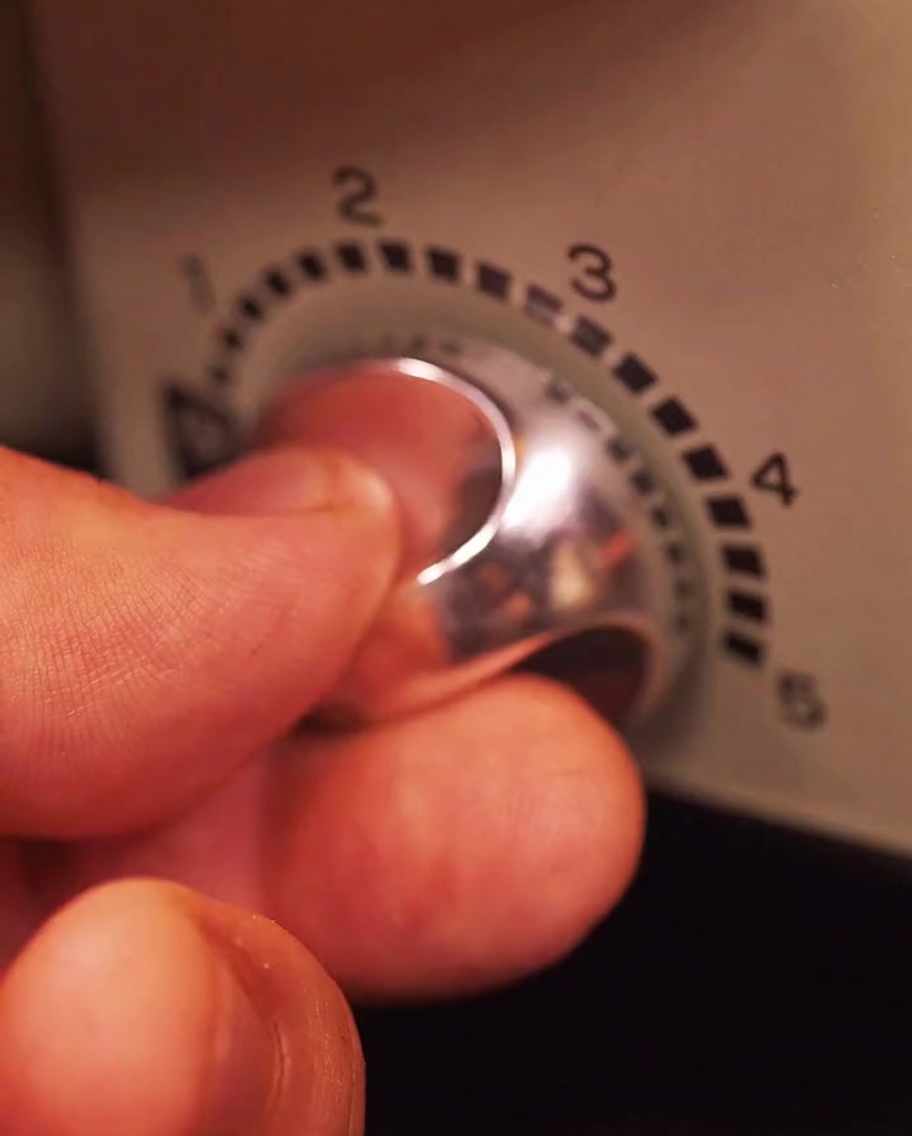 電気グリルの温度調節ダイヤルを手で回して熱を上げている様子。