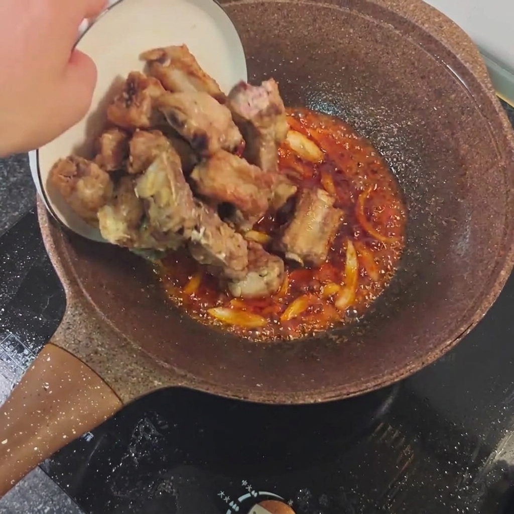 焼いたスペアリブをスパイシーソースに絡めている様子。