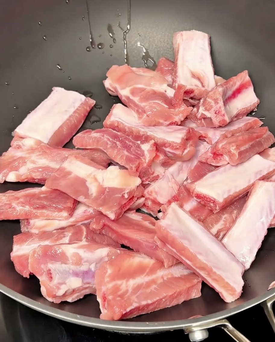 鍋で香味野菜と一緒に湯通しされている豚スペアリブ。