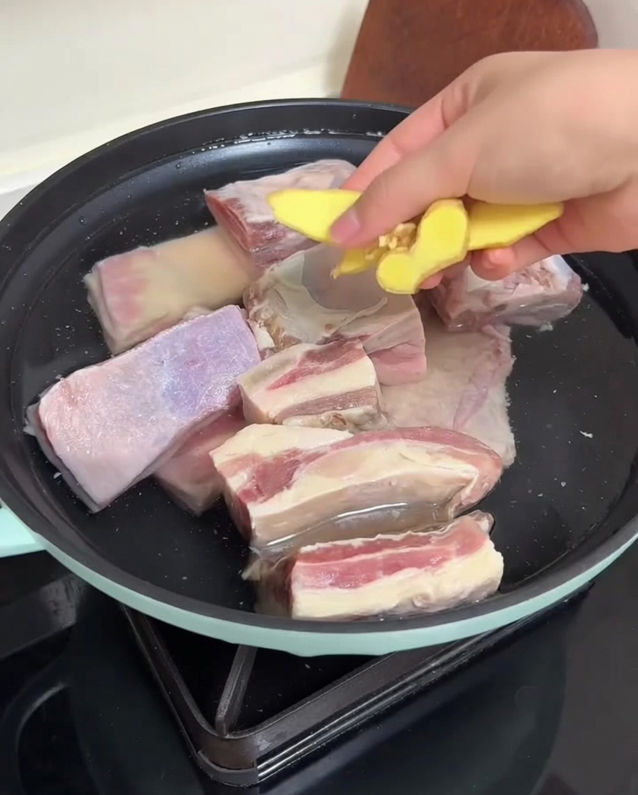 鍋に入った水と生姜のスライスと一緒に下茹でされる準備をしている牛カルビ肉。