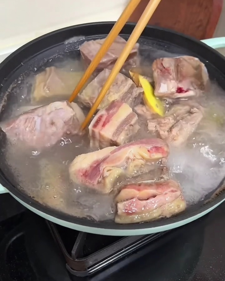 流水の下で、箸を使って下茹でされた牛カルビ肉を丁寧に洗っている手。