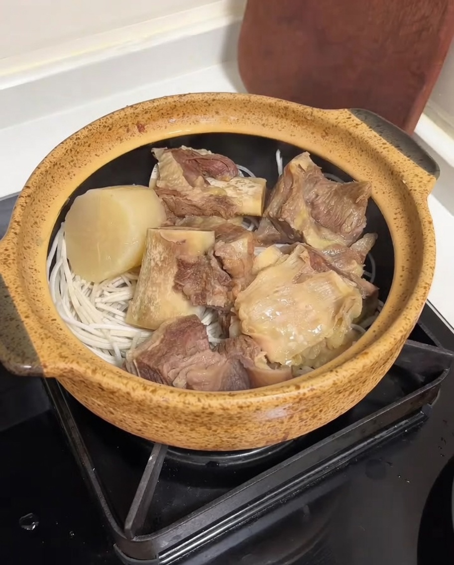 炊飯器から、牛肉、大根、春雨が入った陶製のポットへ、透明で濃厚な牛骨スープが注がれている様子。