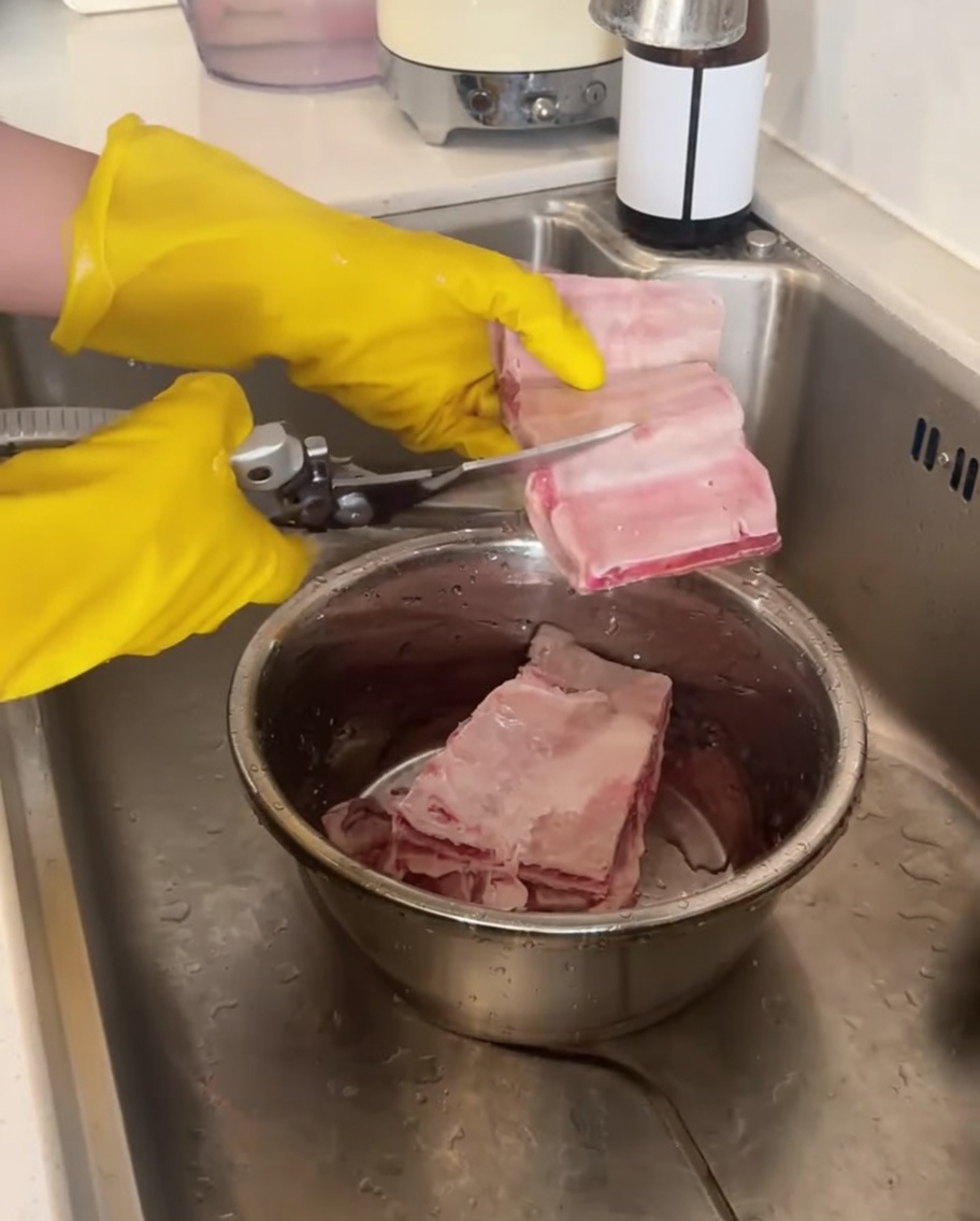 黄色いゴム手袋をした手が、キッチンバサミで生のカルビを切り分けている様子。