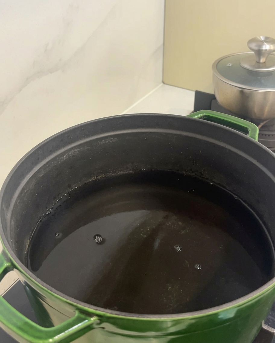 大きな緑色の鍋に冷たい水と生の牛カルビが入っている様子。