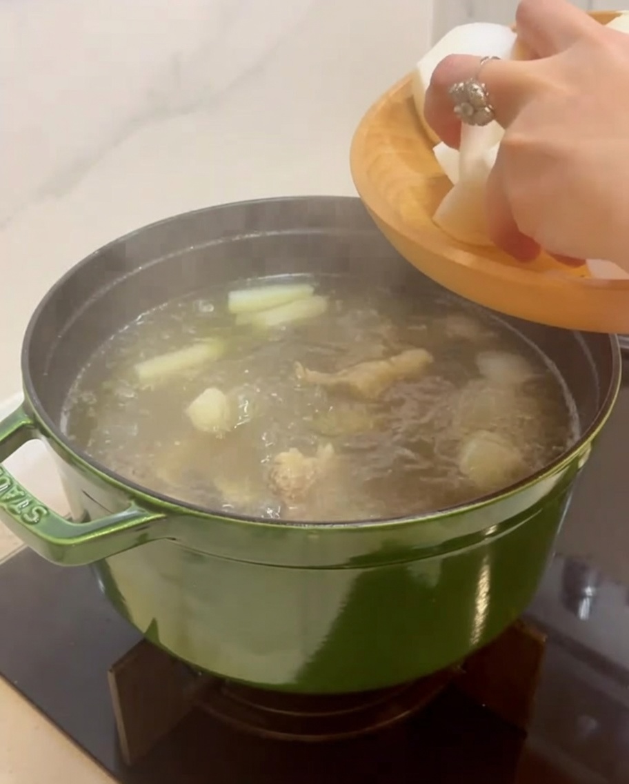 皮をむいた韓国大根の大きな塊を、煮込んでいるスープ鍋に手で入れている様子。