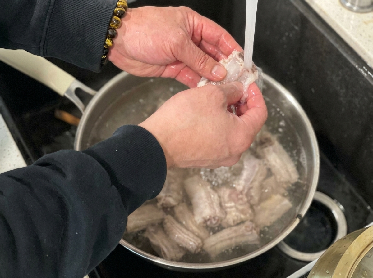 下茹でしたスペアリブを蛇口からの流水で丁寧に洗っている様子。