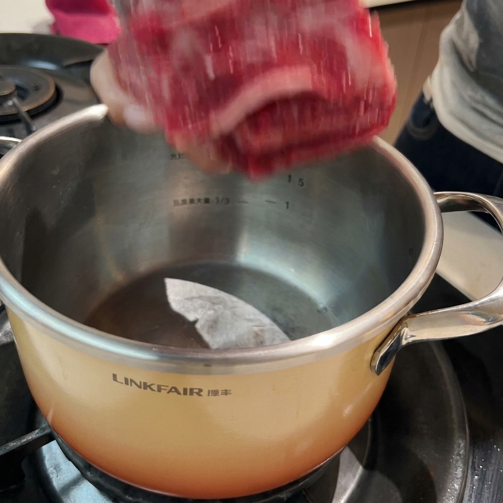 鍋の中で生姜やネギと一緒に冷水から茹でられる牛カルビ。