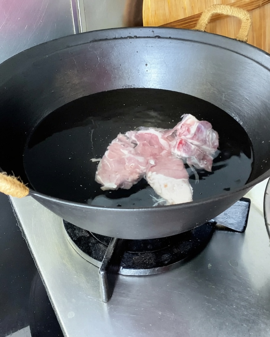 鍋に豚背骨、生姜、ネギ、料理酒を入れて茹でている様子。