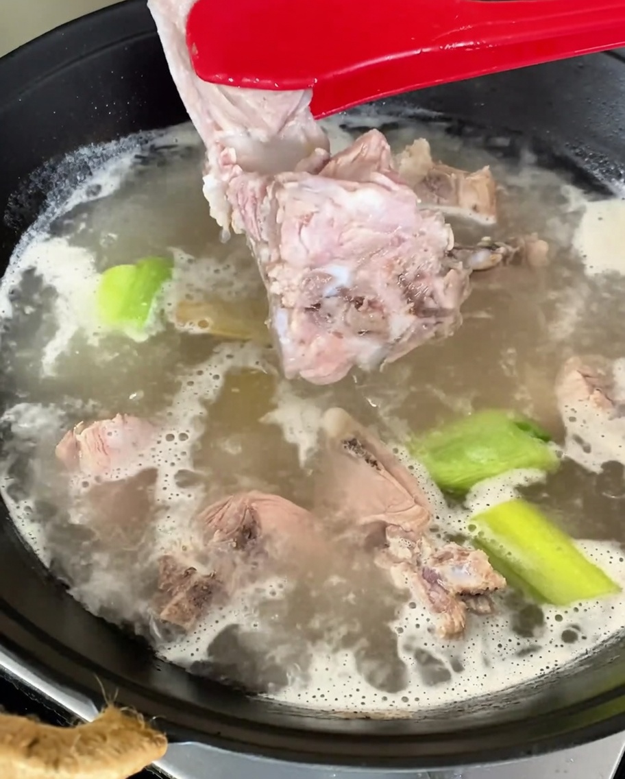 茹で上がった豚背骨をトングで取り出している様子。