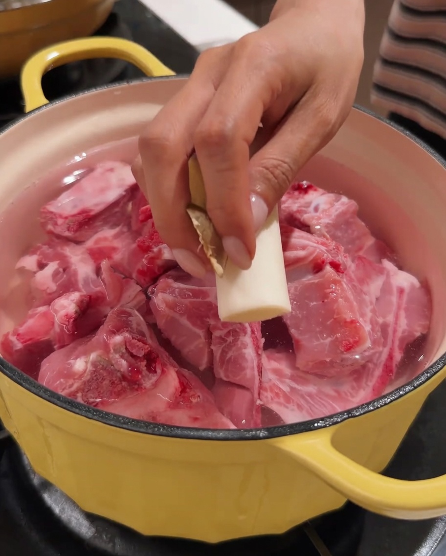 豚背骨と水が入った鍋に生姜の切れ端を入れている手