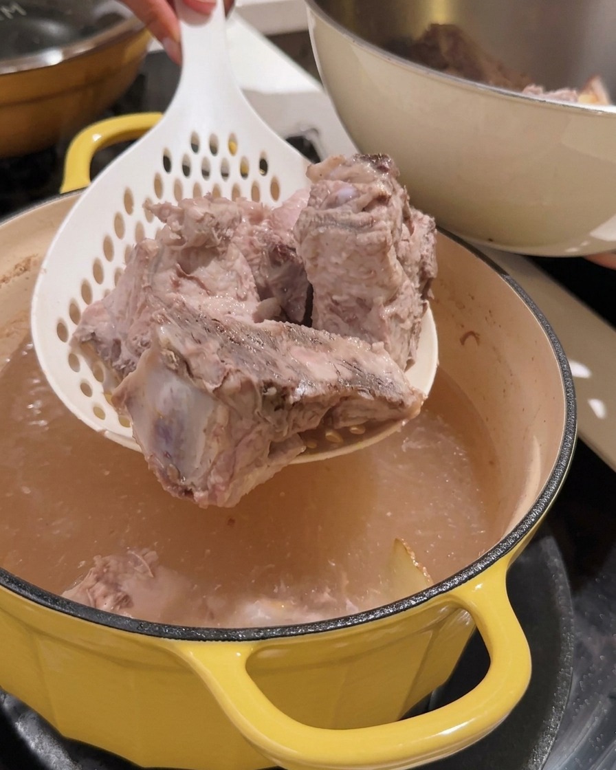ザルを使って鍋から下茹でされた豚背骨を取り出している様子