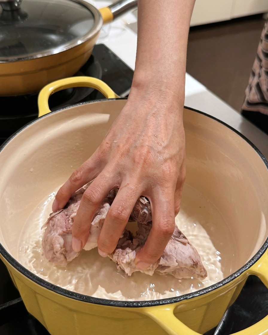 綺麗に洗った豚背骨の塊を空の煮込み鍋に戻し入れている手