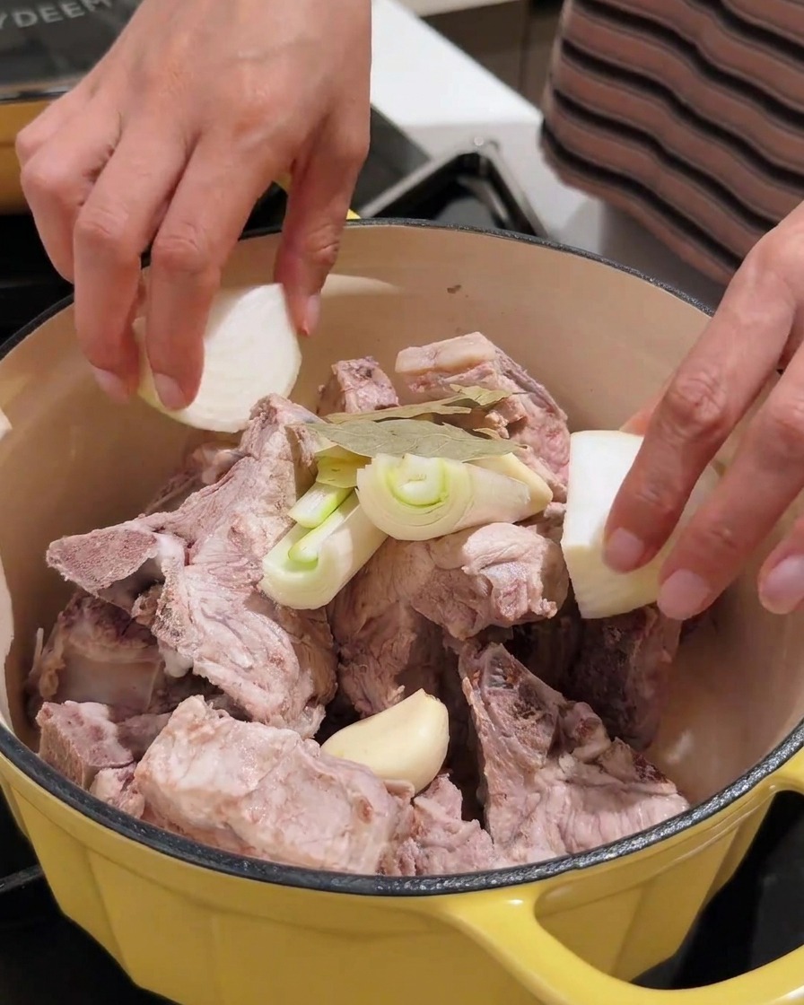 ニンニク、玉ねぎ、味噌などの香味野菜が豚肉の入った鍋に加えられている様子