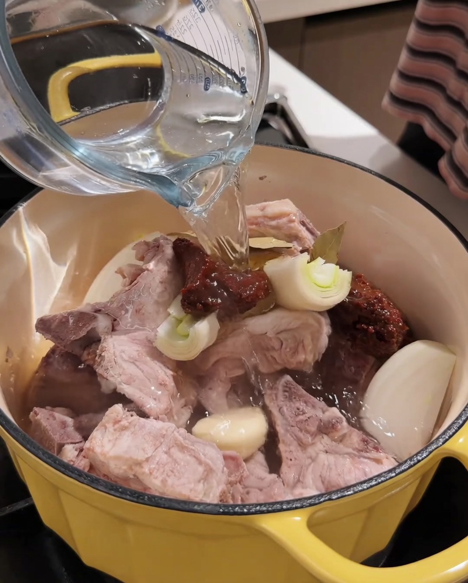 計量カップから豚肉と調味料の入った鍋にお湯を注いでいる様子
