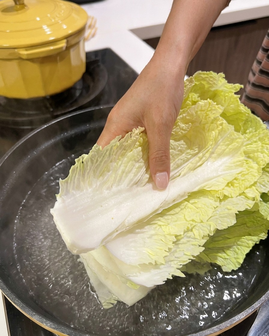 コンロの上の沸騰したお湯の鍋に、生白菜の葉を入れている様子
