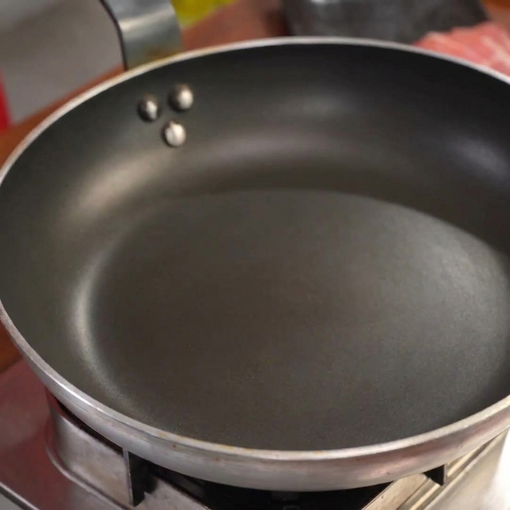 油や水を入れずに予熱したフライパンに入っている生の豚バラ肉のスライス。