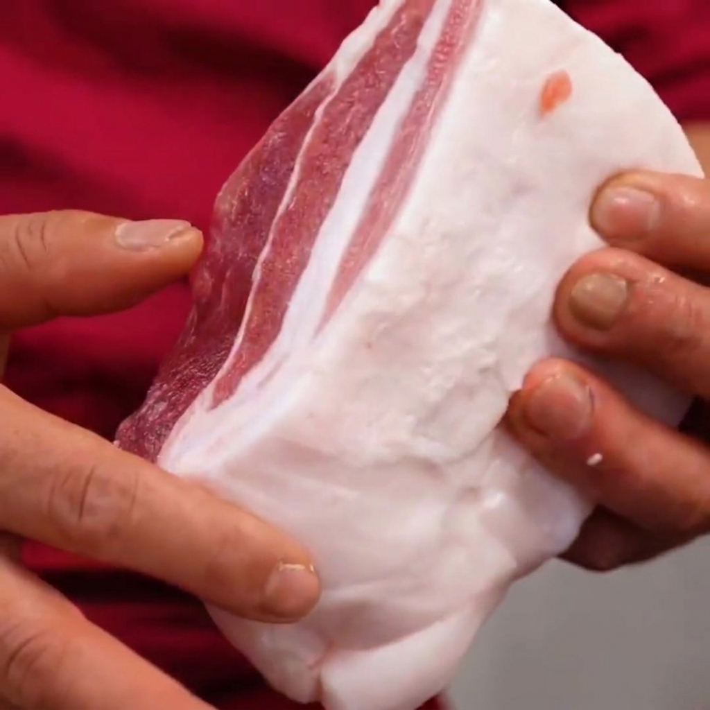 両手で豚バラ肉を持ち、45度の角度で切り込みを入れている様子。