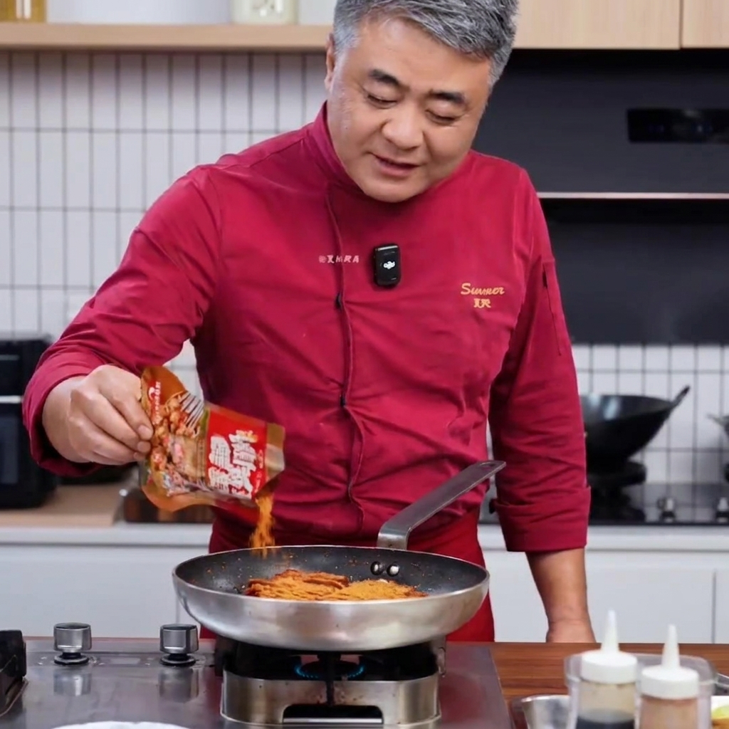 赤い服を着たシェフが、焼いた肉が入ったフライパンにスパイスを振りかけている様子。