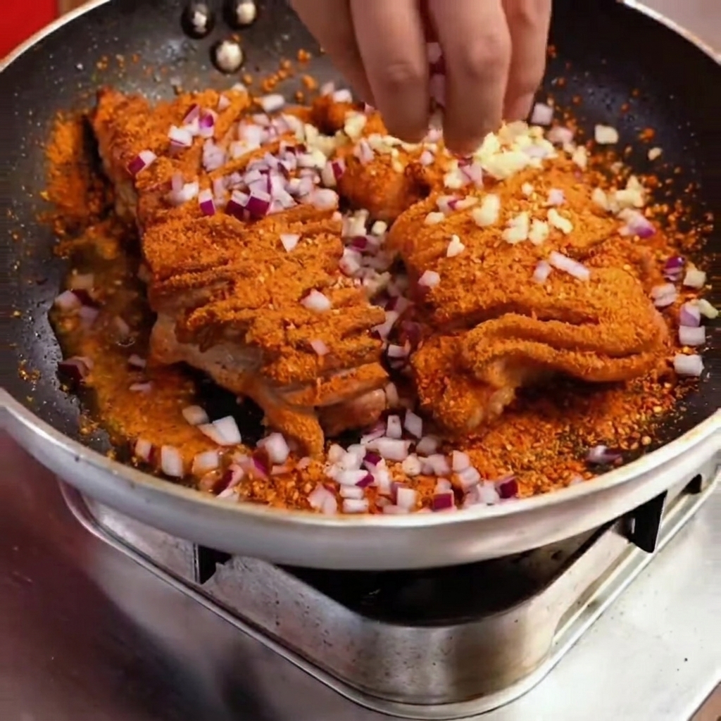 スパイスで焼かれた肉の上に、刻んだ赤玉ねぎとピーマンを加えて調理している様子。